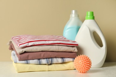 Photo of Orange dryer ball, laundry detergents and stacked clean clothes on white table