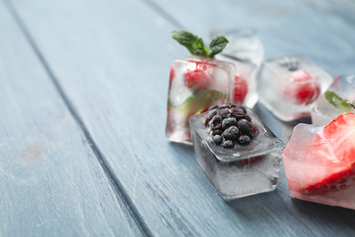 Photo of Ice cubes with different berries and mint on blue wooden table, closeup. Space for text