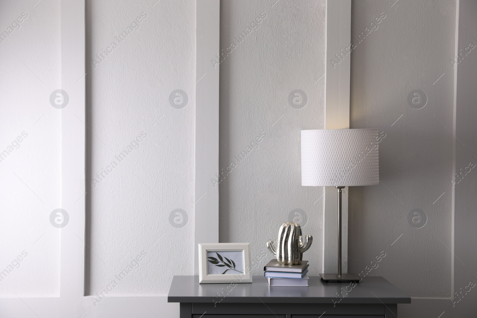 Photo of Wooden table with books, decor and lamp near white wall in room, space for text