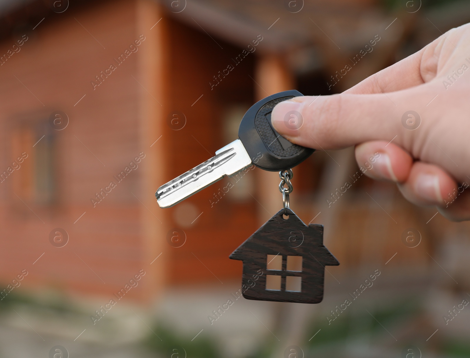 Photo of Real estate agent holding key and blurred house on background. Focus on hand