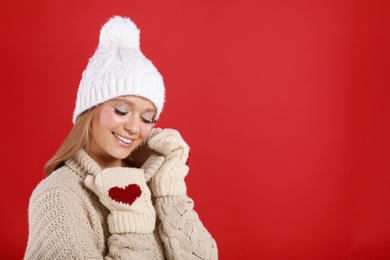 Photo of Young woman in warm sweater, mittens and hat on red background, space for text. Winter season