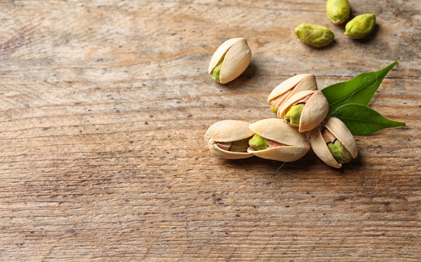 Photo of Organic pistachio nuts on wooden table. Space for text