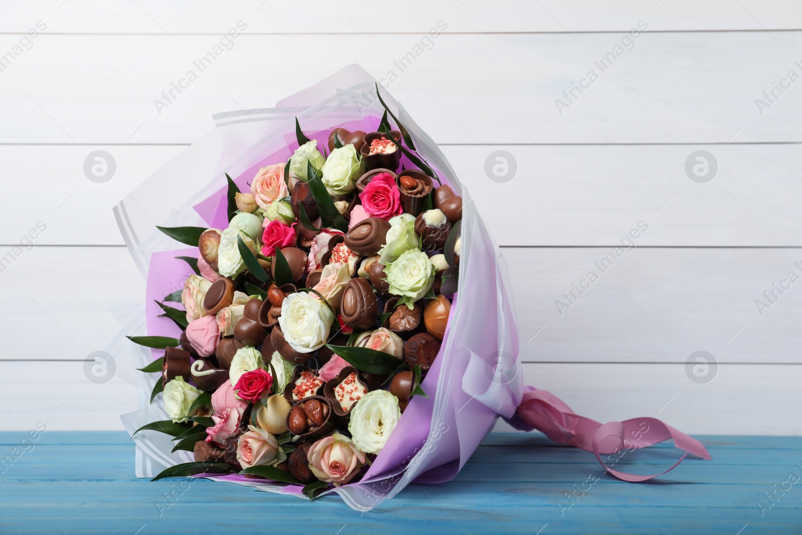 Photo of Beautiful bouquet of flowers and chocolate candies on light blue table against white wooden background