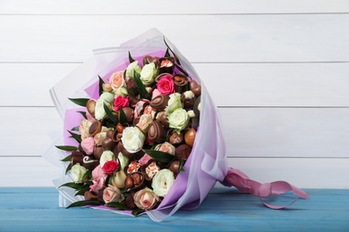 Beautiful bouquet of flowers and chocolate candies on light blue table against white wooden background