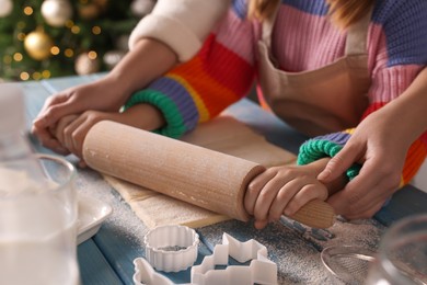 Photo of Mother and child rolling dough for Christmas cookies at blue wooden table together, closeup