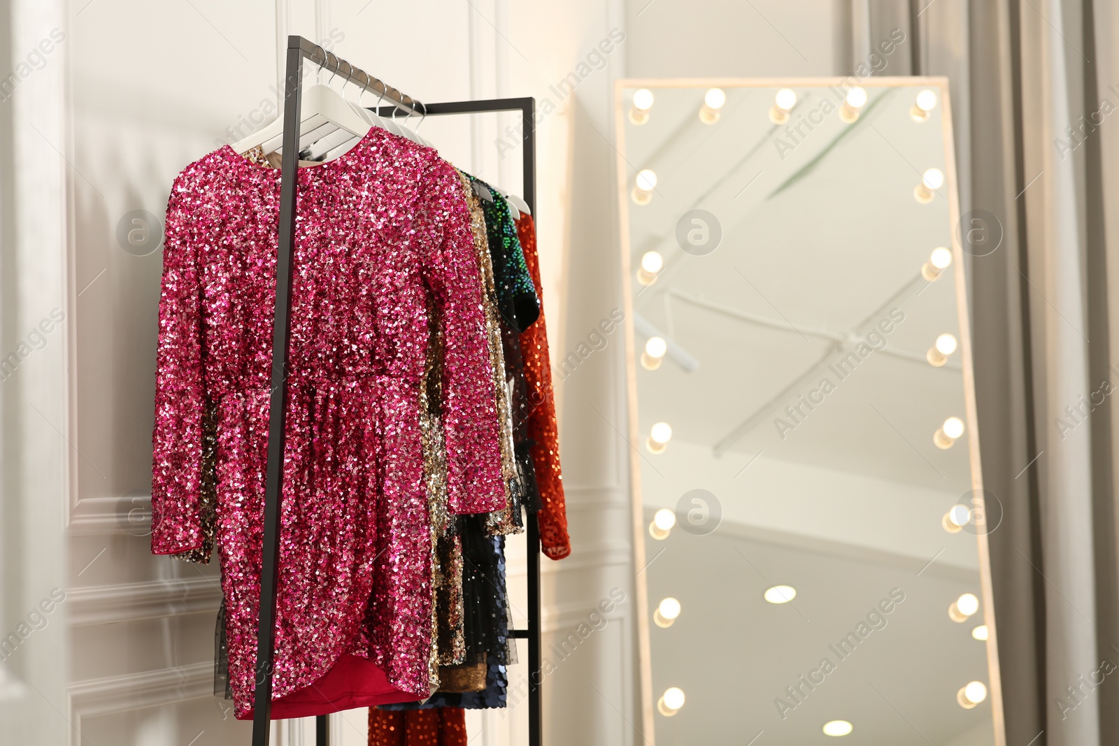 Photo of Clothing rack with colorful sequin party dresses on hangers near mirror in boutique, space for text