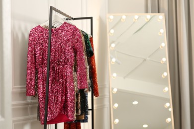 Photo of Clothing rack with colorful sequin party dresses on hangers near mirror in boutique, space for text