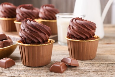 Photo of Delicious cupcakes and chocolate pieces on wooden table, closeup