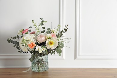 Photo of Bouquet of beautiful flowers in vase on wooden table near white wall. Space for text