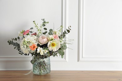 Bouquet of beautiful flowers in vase on wooden table near white wall. Space for text