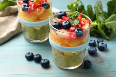 Delicious fruit salad in glasses, fresh berries and mint on light blue wooden table