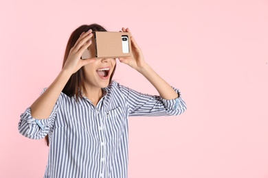 Photo of Young woman using cardboard virtual reality headset on color background. Space for text