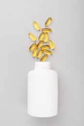 Bottle and vitamin capsules on light grey background, top view