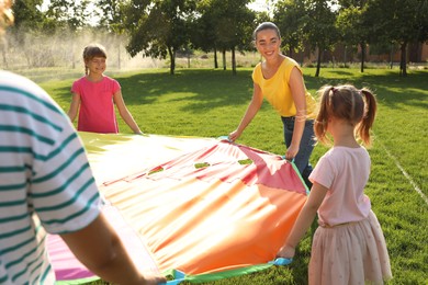 Photo of Group of children and teacher playing with rainbow playground parachute on green grass. Summer camp activity