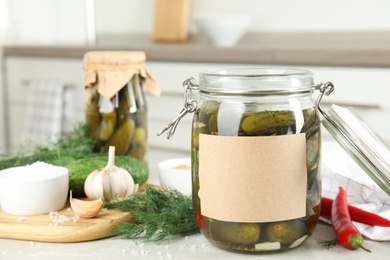 Jar of pickled cucumbers with blank sticker on grey table in kitchen, space for text