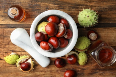 Photo of Mortar with pestle, chestnuts and essential oil on wooden table, flat lay