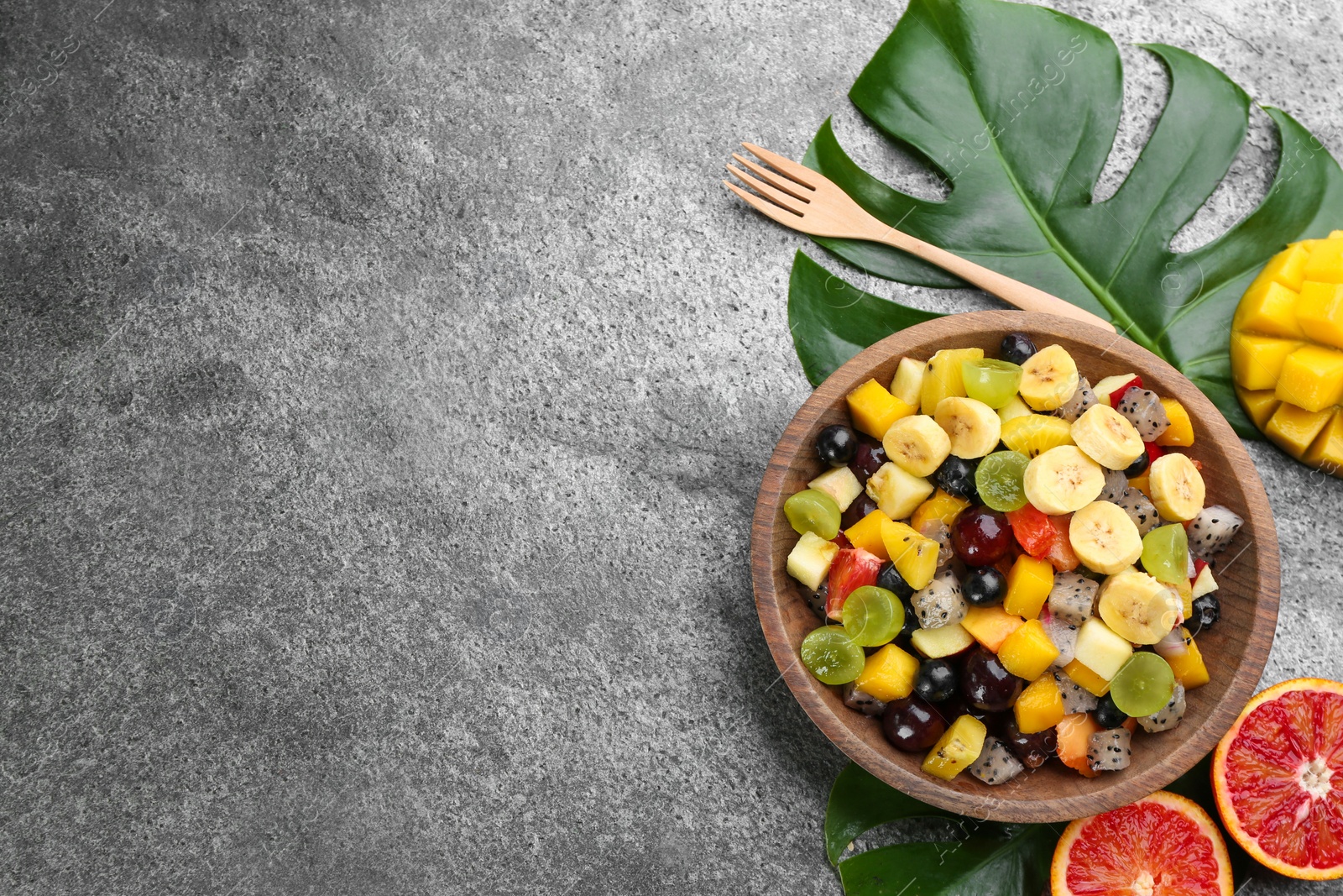 Photo of Delicious exotic fruit salad on grey table, flat lay. Space for text