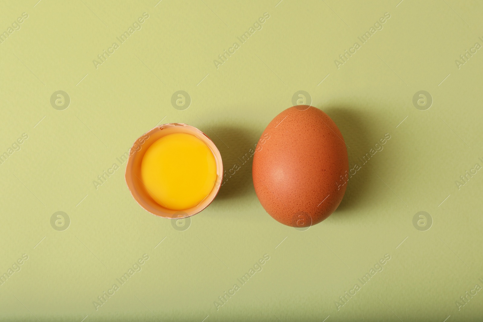 Photo of Cracked and whole chicken eggs on olive background, flat lay