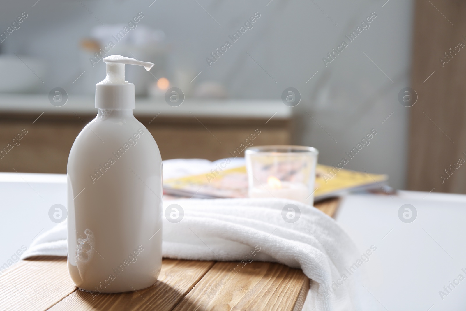 Photo of Wooden bath tray with shower gel, candle and fresh towel on tub indoors. Space for text