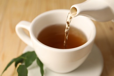 Photo of Pouring tasty tea into cup at table, closeup