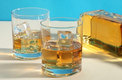 Photo of Whiskey with ice cubes in glasses and bottle on white table, closeup