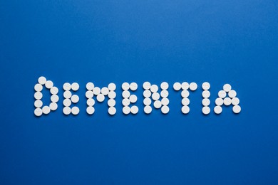 Photo of Word Dementia made of pills on blue background, flat lay