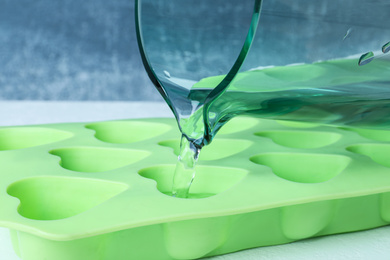 Photo of Pouring water into ice cube tray on table, closeup