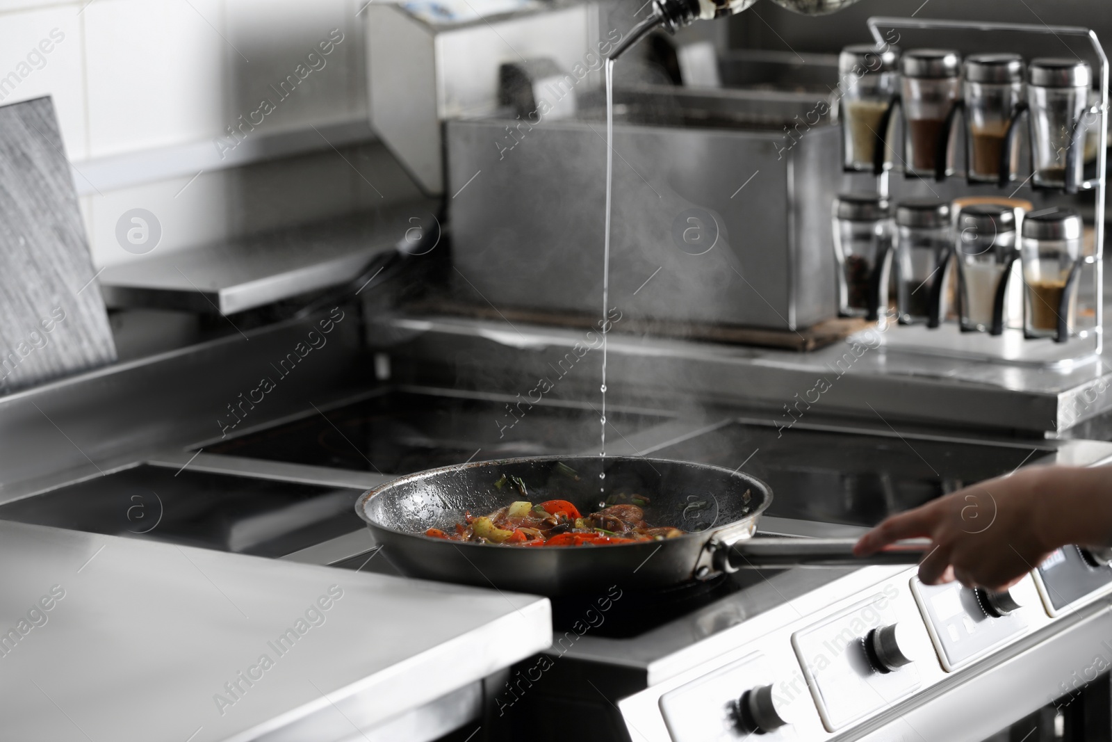 Photo of Woman adding oil to cooking food in restaurant kitchen, closeup