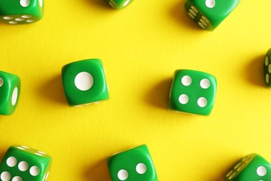 Many green game dices on yellow background, flat lay