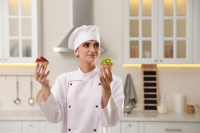 Photo of Happy professional confectioner with delicious tartlets in kitchen