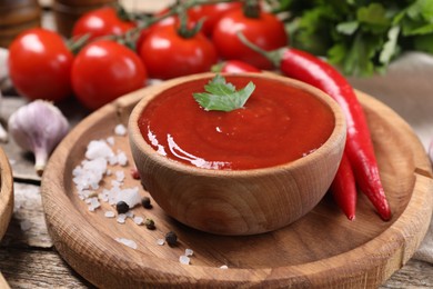 Photo of Delicious ketchup in bowl and spices on wooden table, closeup. Tomato sauce
