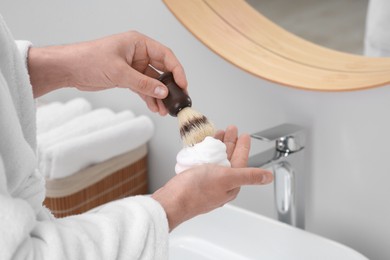 Man applying shaving foam onto brush in bathroom, closeup