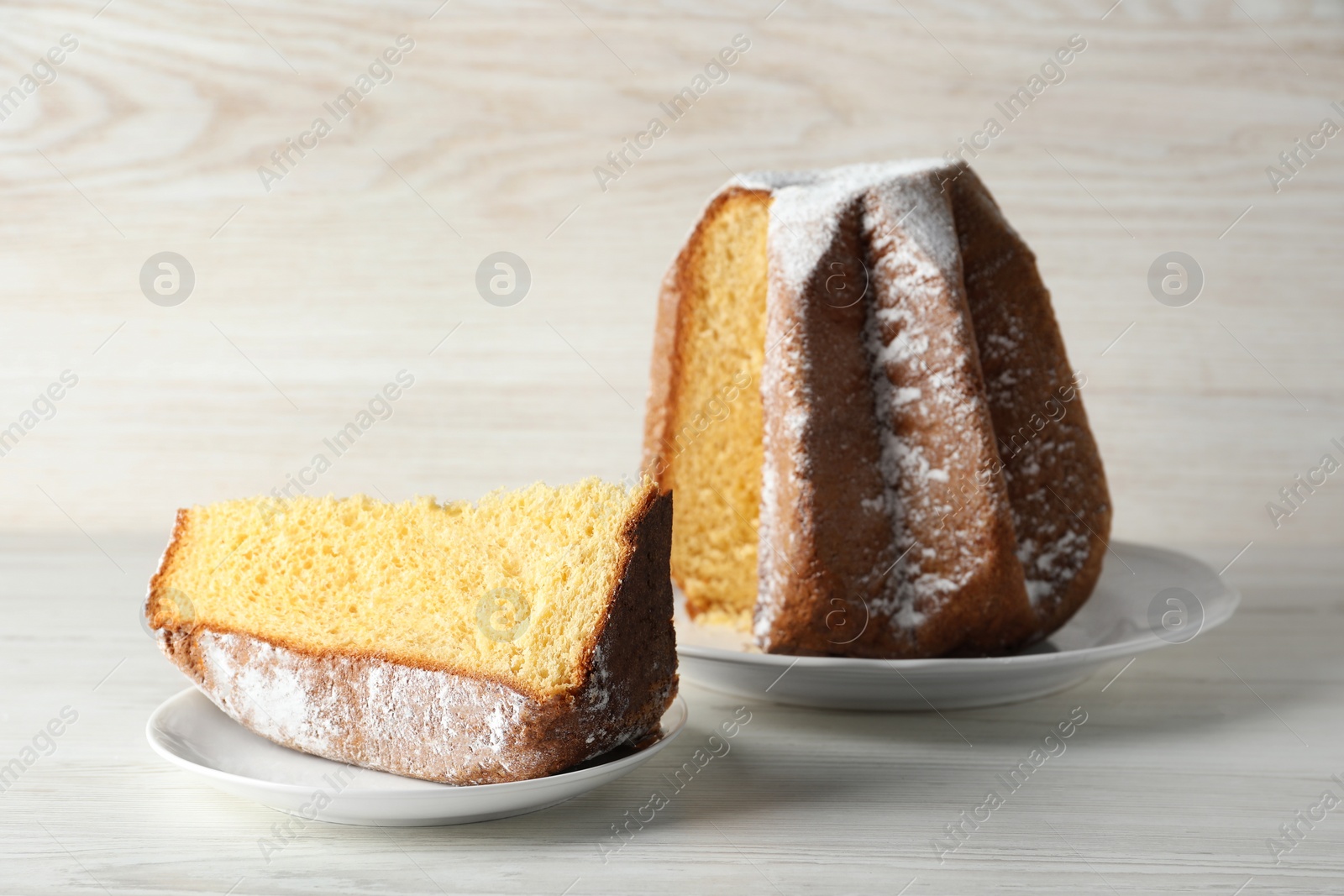 Photo of Delicious Pandoro cake decorated with powdered sugar on white wooden table. Traditional Italian pastry