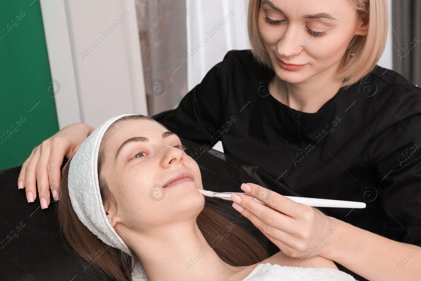 Photo of Cosmetologist applying mask on woman's face in clinic