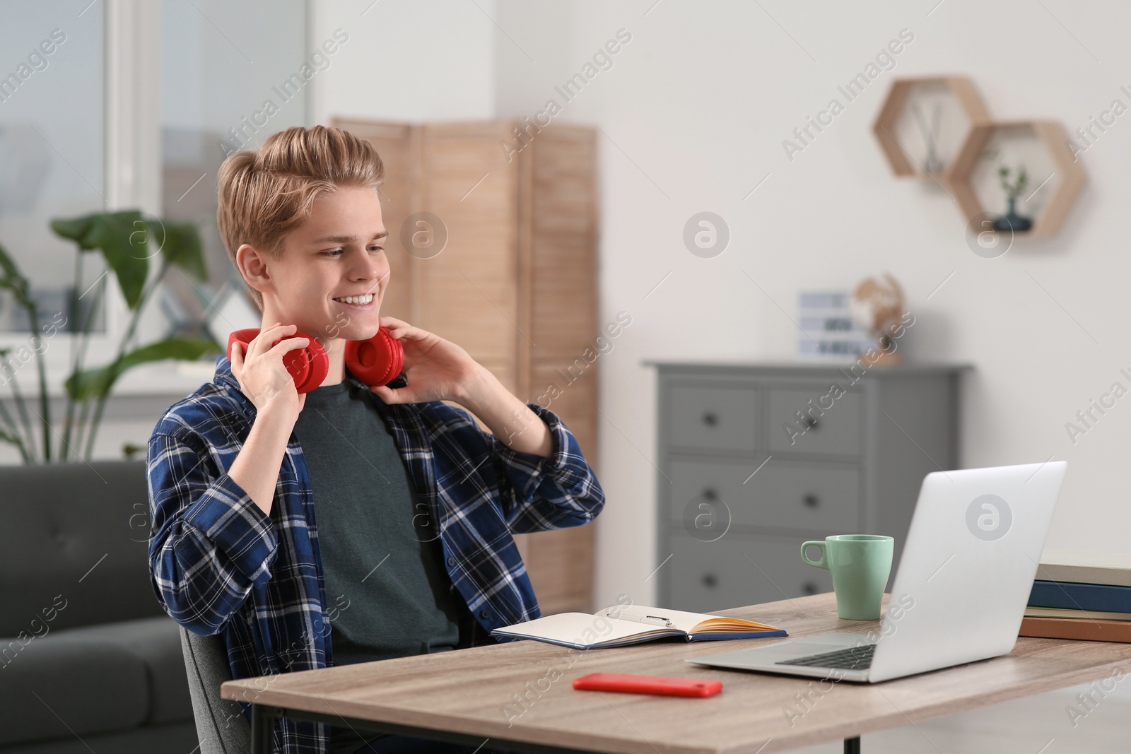 Photo of Online learning. Smiling teenage boy near laptop at home