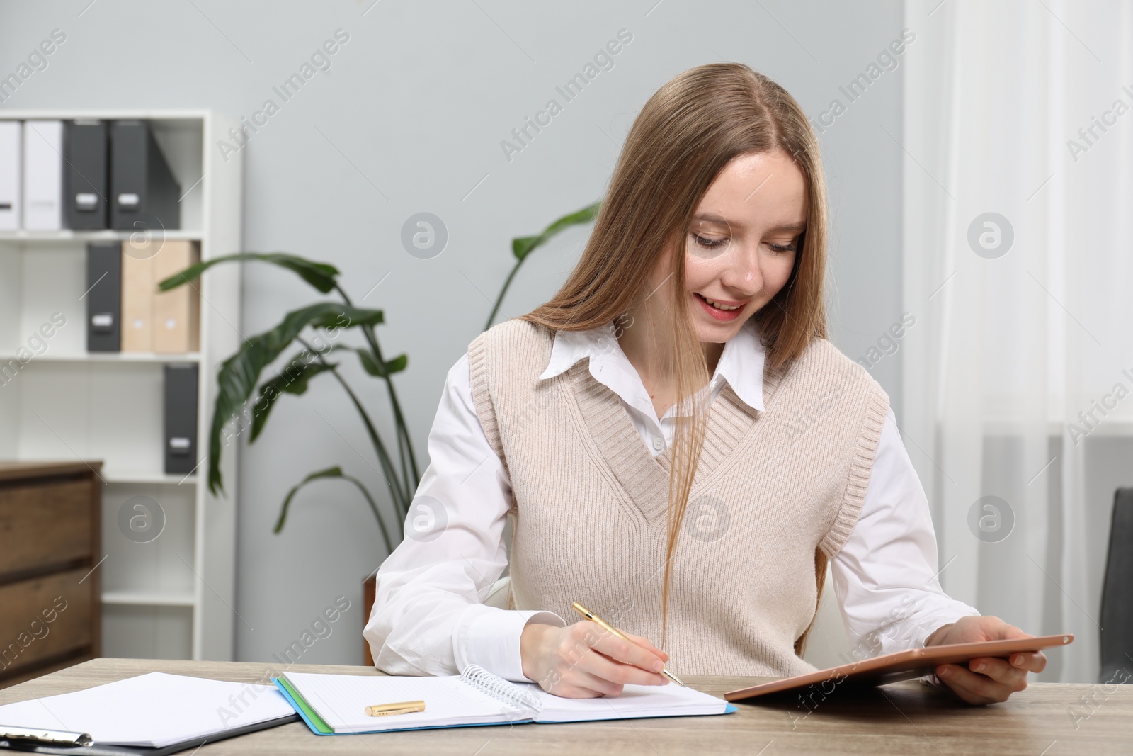 Photo of Woman taking notes while using tablet at wooden table in office, space for text