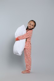 Cute girl in pajamas with pillow on light grey background