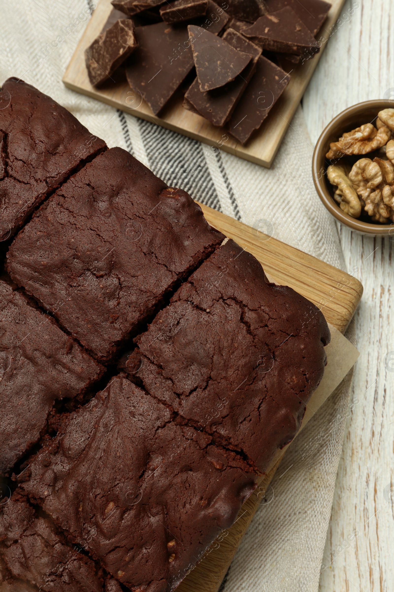 Photo of Delicious freshly baked brownies, walnuts and pieces of chocolate on white wooden table, flat lay