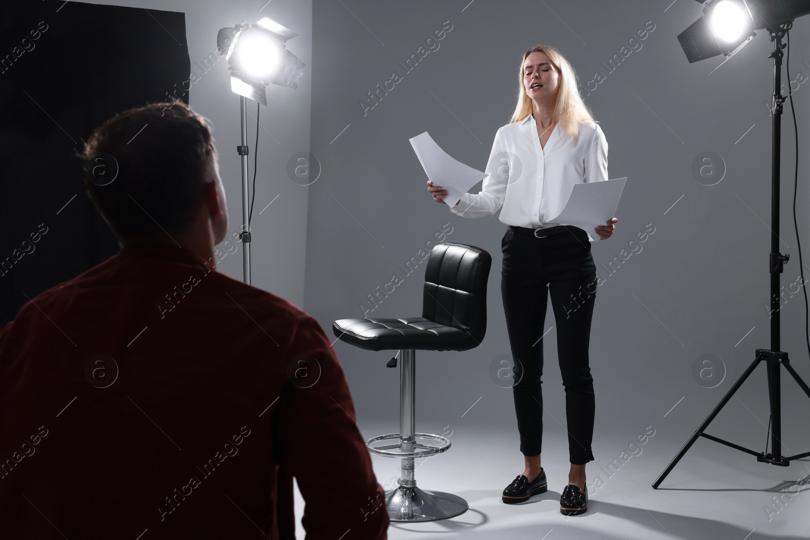 Photo of Emotional woman with script performing in front of casting director against grey background in studio