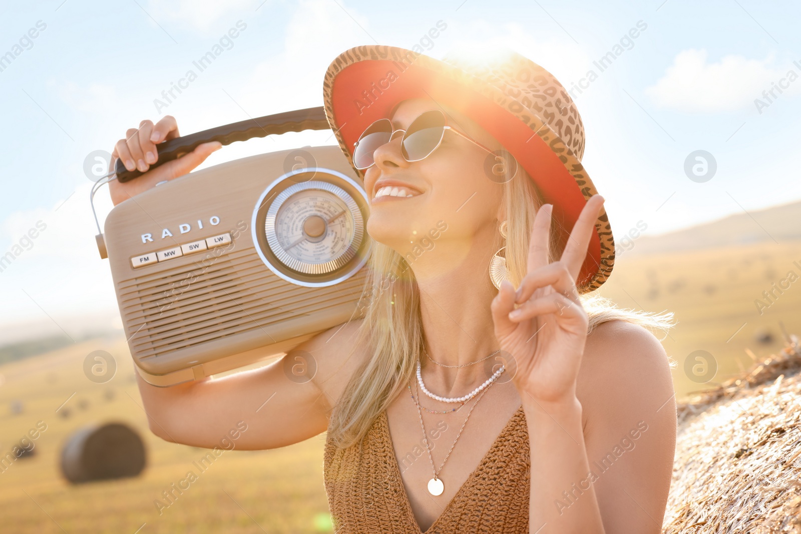 Photo of Happy hippie woman with radio receiver showing peace sign in field