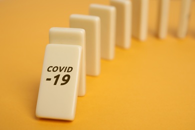 Photo of Domino tiles on yellow background, closeup. Spreading of coronavirus concept