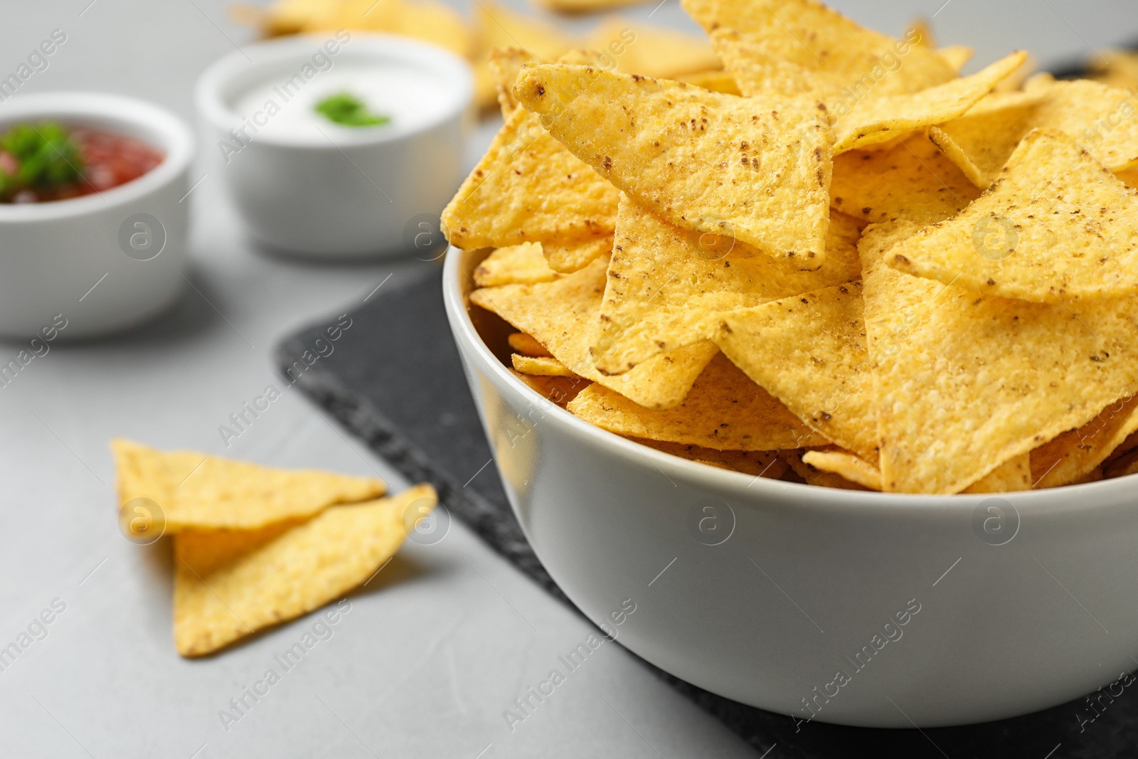 Photo of Bowl with tasty Mexican nachos chips on grey table, closeup view. Space for text