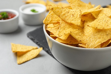 Photo of Bowl with tasty Mexican nachos chips on grey table, closeup view. Space for text