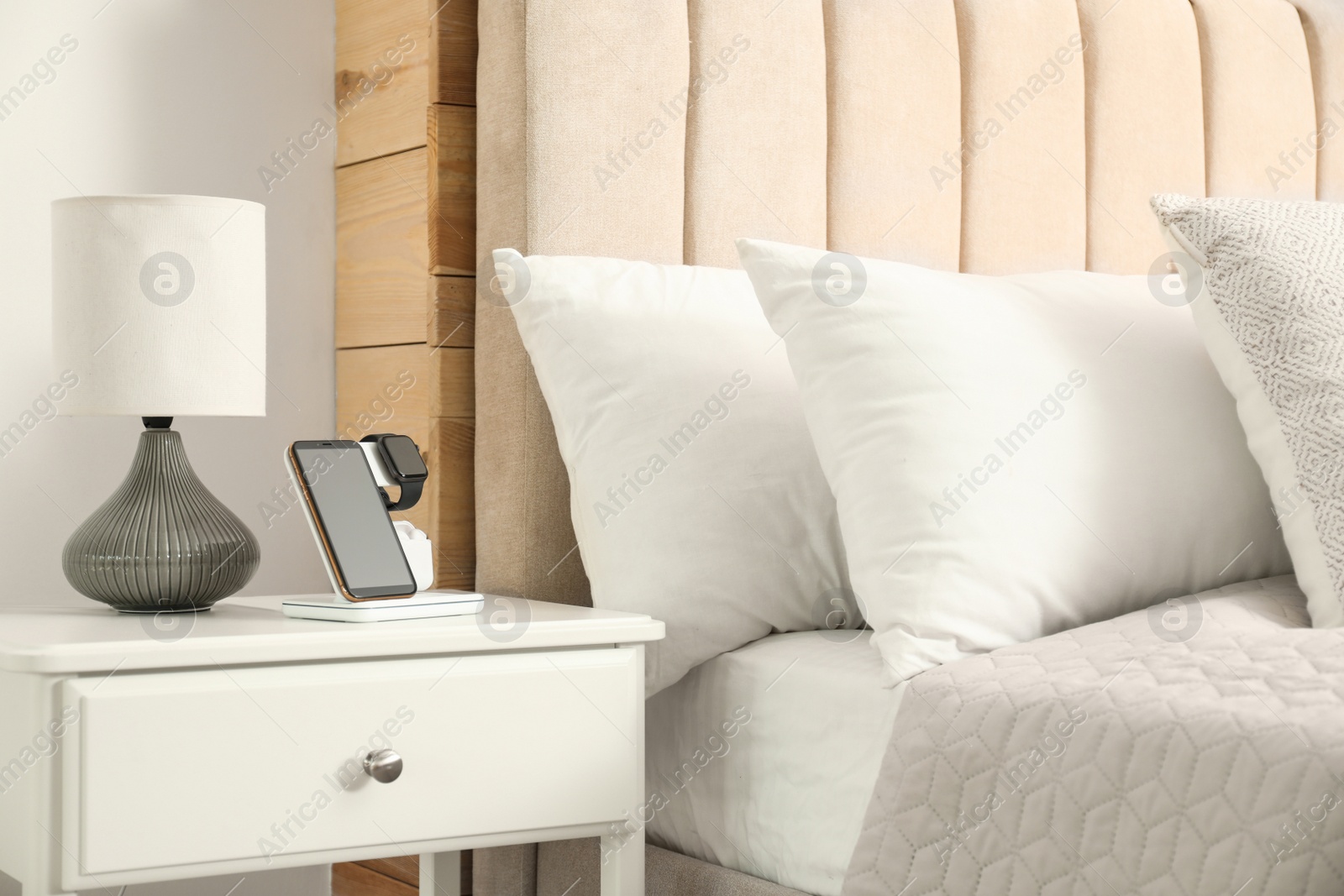 Photo of Different gadgets charging on wireless pad in bedroom