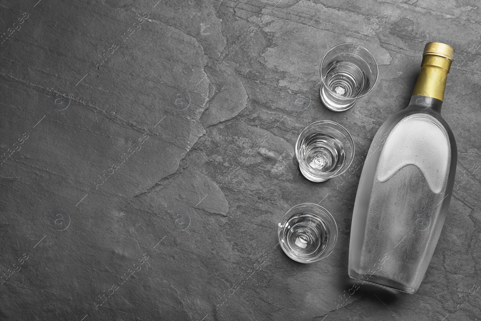 Photo of Bottle of vodka and shot glasses on black table, flat lay. Space for text