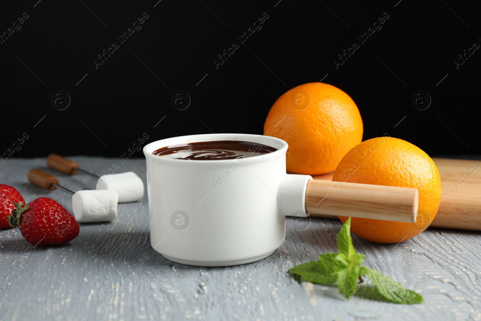 Photo of Fondue pot with chocolate, fruits and marshmallow on grey wooden table