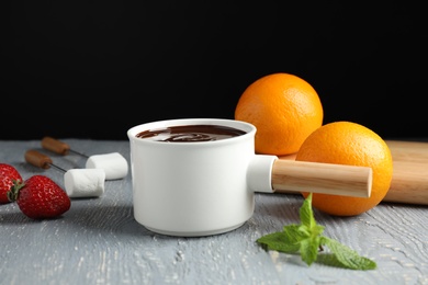 Photo of Fondue pot with chocolate, fruits and marshmallow on grey wooden table