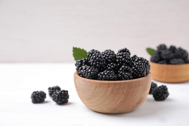 Photo of Fresh ripe blackberries in bowl on white wooden table. Space for text