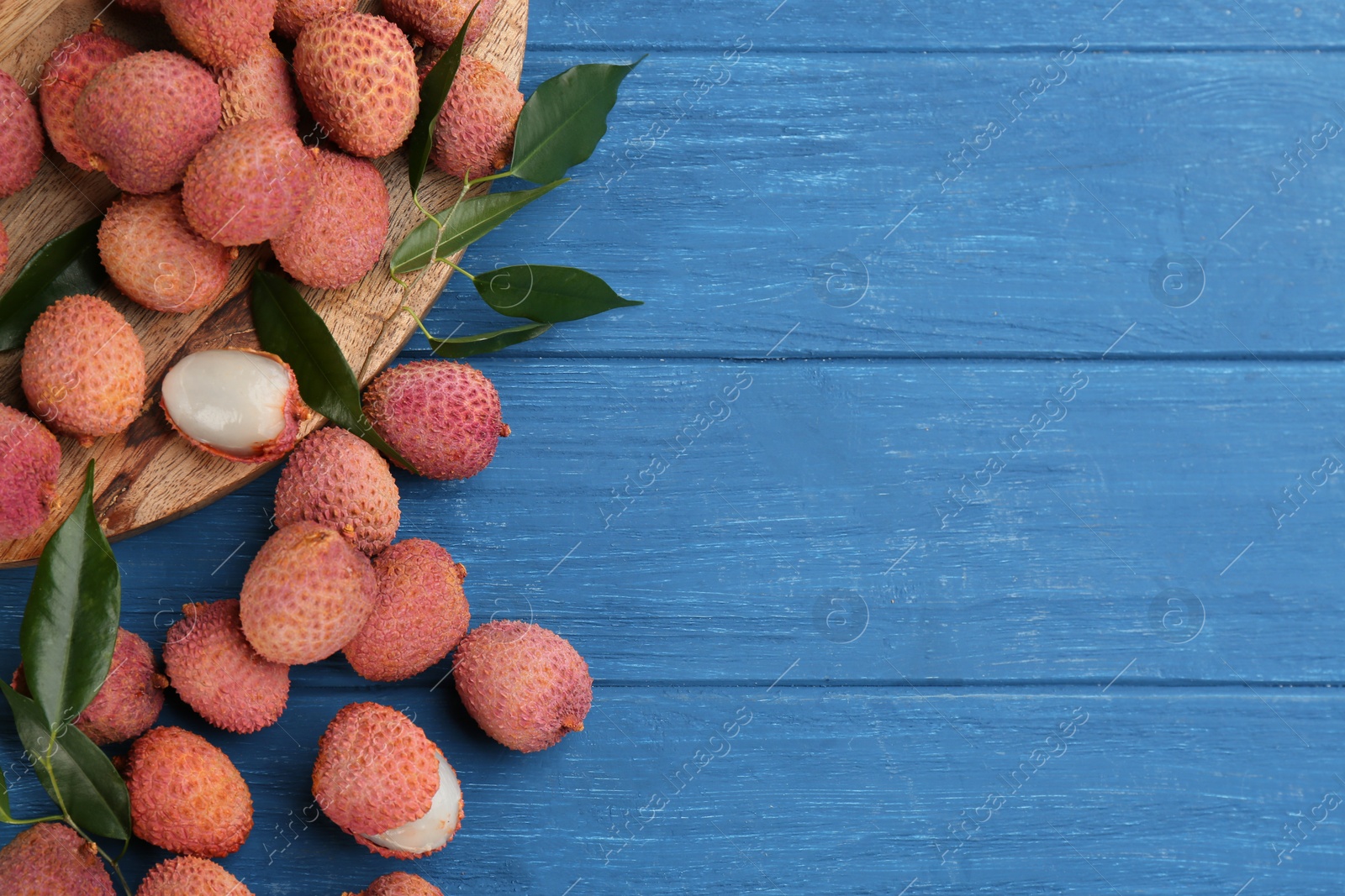 Photo of Fresh ripe lychee fruits on blue wooden table, flat lay. Space for text