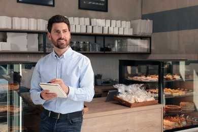 Photo of Happy business owner with notebook and pen in bakery shop